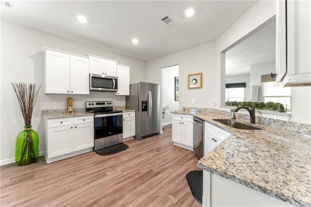 kitchen with light hardwood / wood-style floors, white cabinetry, light stone counters, stainless steel appliances, and sink