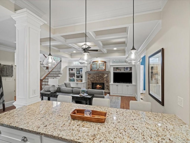 kitchen with coffered ceiling, white cabinetry, hanging light fixtures, a fireplace, and light stone countertops