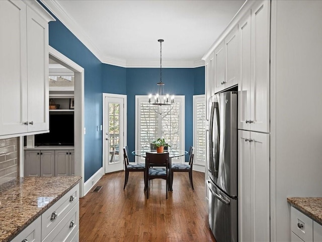 kitchen with crown molding, stainless steel refrigerator, pendant lighting, light stone countertops, and white cabinets