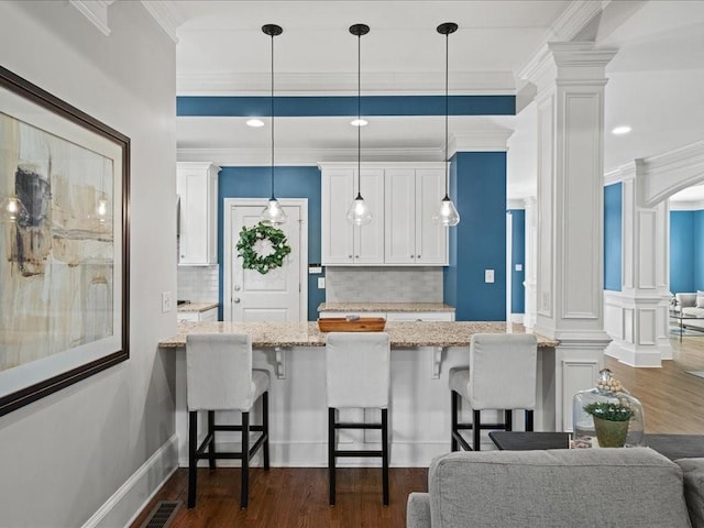 kitchen featuring a kitchen breakfast bar, light stone countertops, white cabinets, decorative light fixtures, and ornate columns