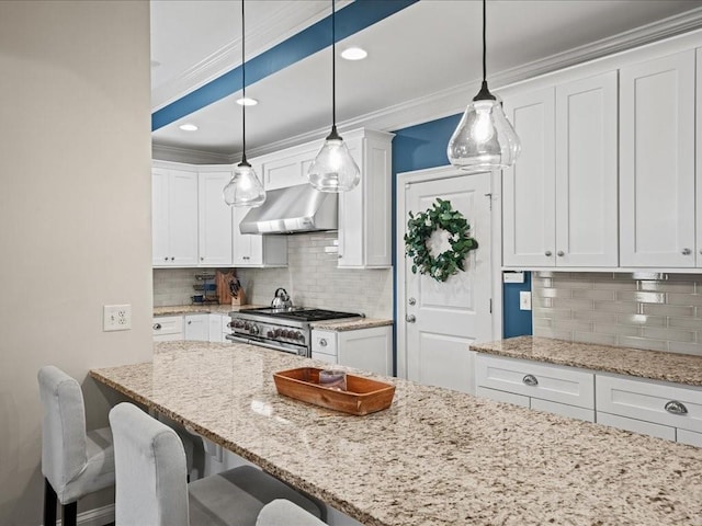 kitchen featuring a breakfast bar, range hood, white cabinets, hanging light fixtures, and high end stainless steel range