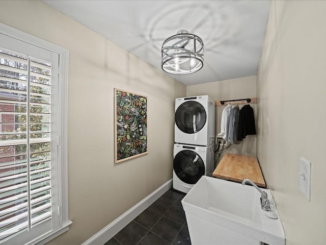 laundry room with an inviting chandelier, stacked washer / dryer, dark tile patterned flooring, and sink