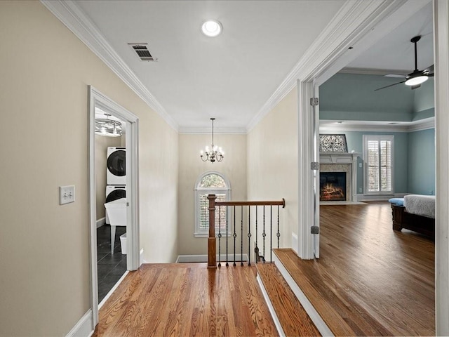 corridor with crown molding, stacked washer and clothes dryer, hardwood / wood-style floors, and a notable chandelier