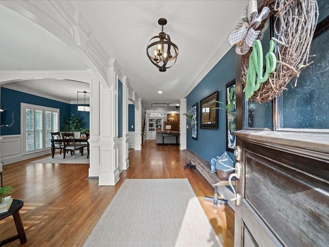 foyer entrance with decorative columns, crown molding, hardwood / wood-style flooring, and a chandelier