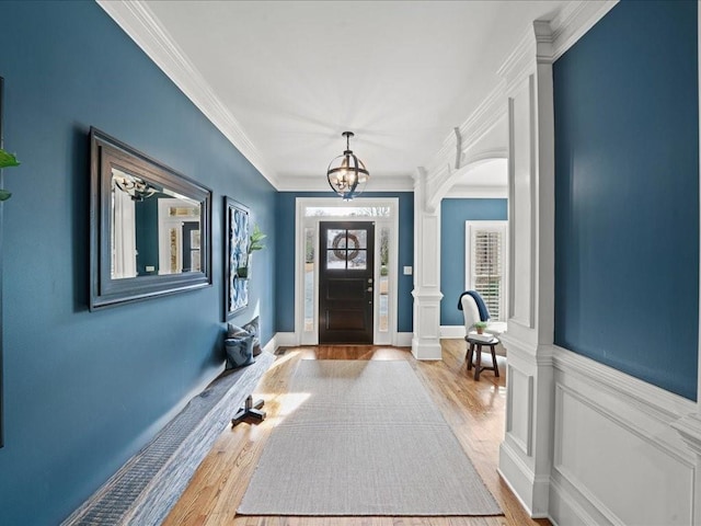 foyer entrance with crown molding, light hardwood / wood-style floors, decorative columns, and a notable chandelier