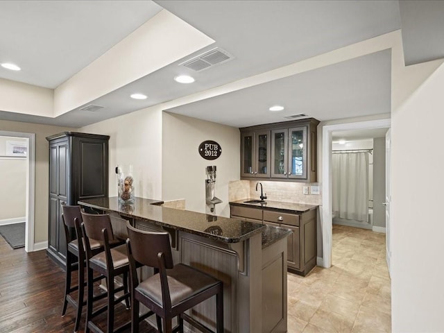 kitchen featuring a breakfast bar, tasteful backsplash, dark stone counters, dark brown cabinetry, and kitchen peninsula