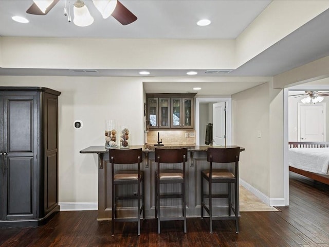 bar with tasteful backsplash, ceiling fan, dark brown cabinetry, and dark hardwood / wood-style flooring