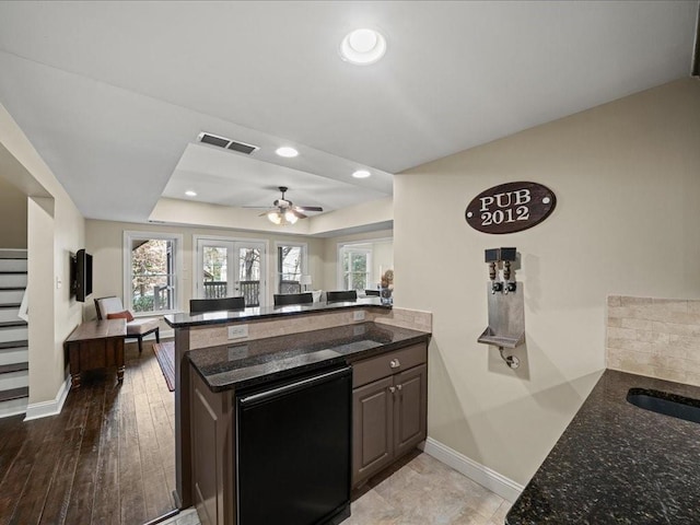 kitchen featuring a raised ceiling, a wealth of natural light, dark stone counters, and kitchen peninsula