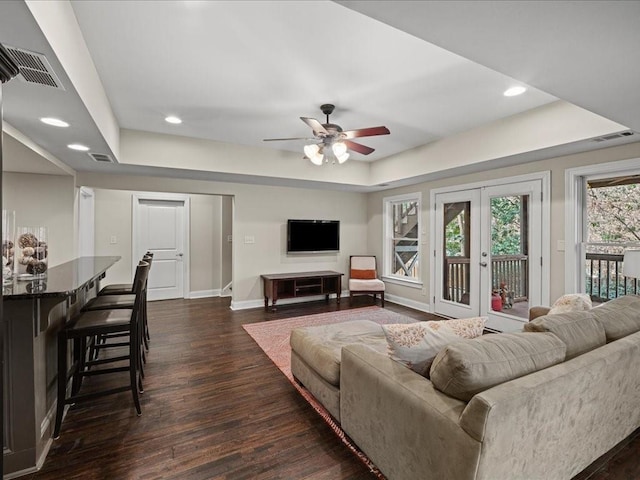 living room with dark wood-type flooring, ceiling fan, a tray ceiling, and french doors