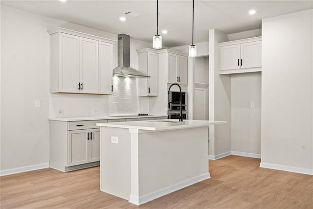 kitchen with a center island with sink, light wood-type flooring, light countertops, wall chimney exhaust hood, and black electric cooktop