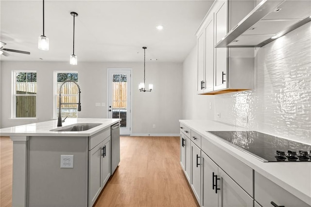 kitchen featuring light wood finished floors, a sink, wall chimney exhaust hood, light countertops, and black electric cooktop