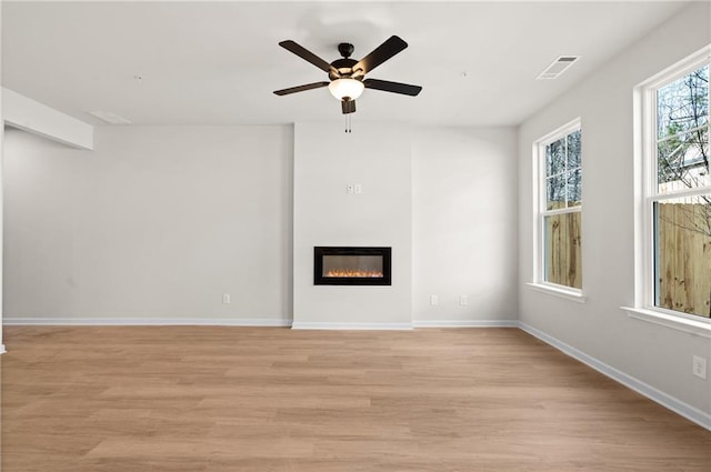 unfurnished living room featuring a ceiling fan, baseboards, visible vents, a glass covered fireplace, and light wood-type flooring