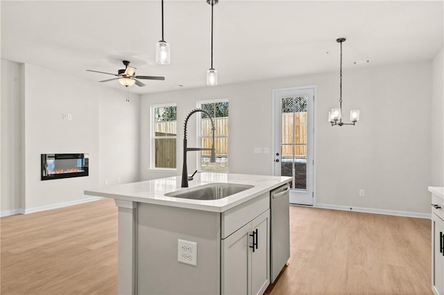 kitchen with light wood finished floors, light countertops, stainless steel dishwasher, a glass covered fireplace, and a sink