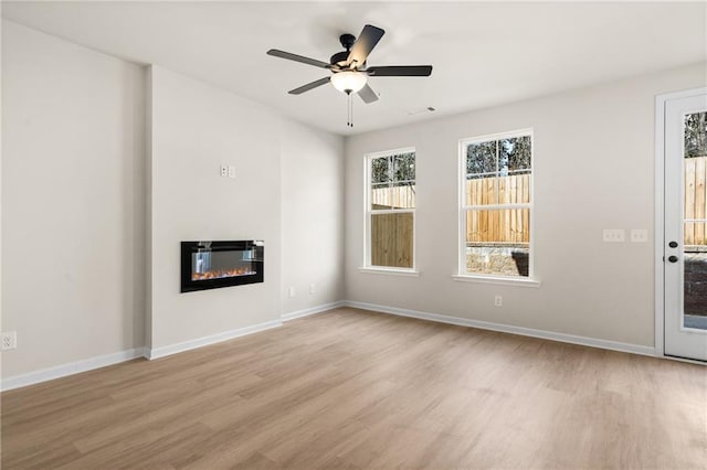 unfurnished living room with visible vents, a ceiling fan, wood finished floors, a glass covered fireplace, and baseboards