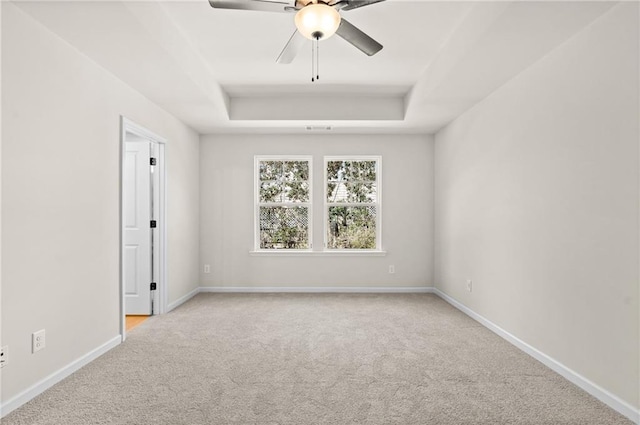 spare room with a tray ceiling, carpet floors, baseboards, and ceiling fan