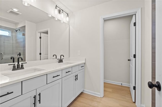 bathroom with a sink, visible vents, wood finished floors, and a shower stall