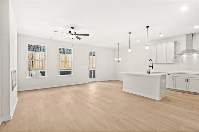 kitchen with a sink, cooktop, light wood-style flooring, and wall chimney range hood