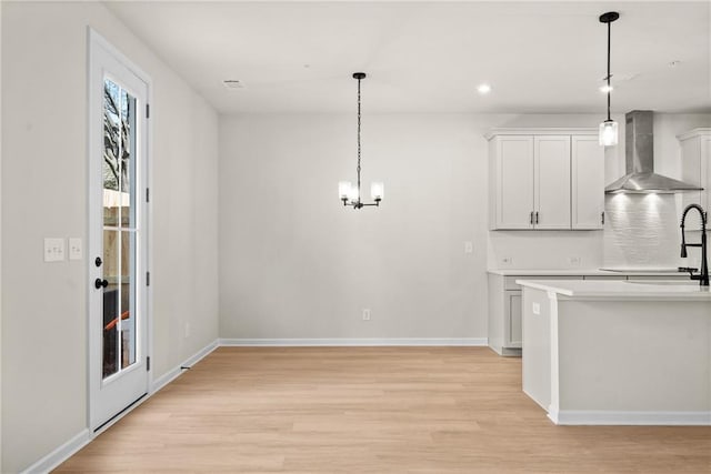 kitchen with light wood-type flooring, baseboards, wall chimney exhaust hood, and hanging light fixtures