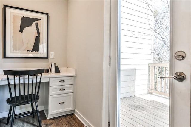 office space featuring dark wood finished floors, built in desk, and baseboards