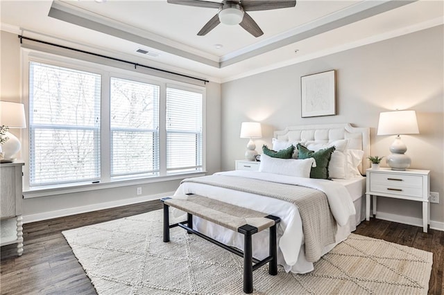 bedroom with a raised ceiling, crown molding, baseboards, dark wood-type flooring, and a ceiling fan