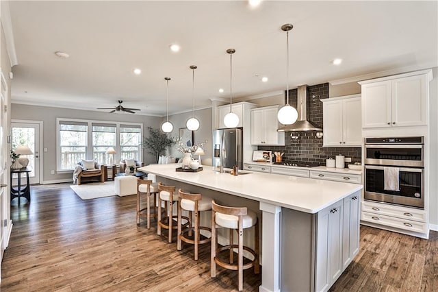 kitchen featuring wall chimney range hood, a spacious island, backsplash, stainless steel appliances, and light countertops