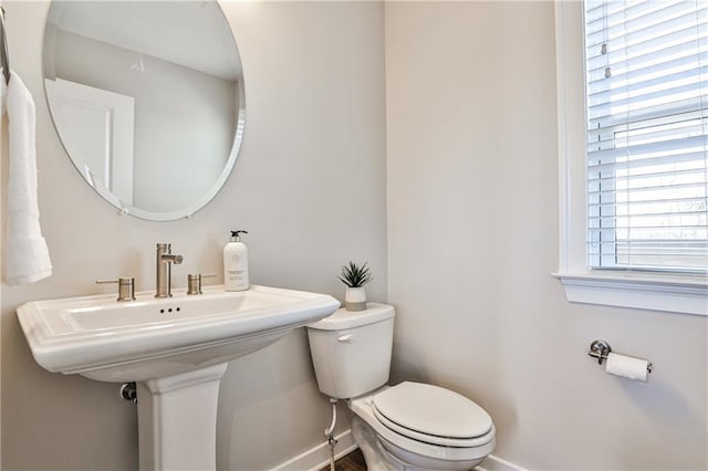 half bathroom with toilet, a healthy amount of sunlight, and baseboards