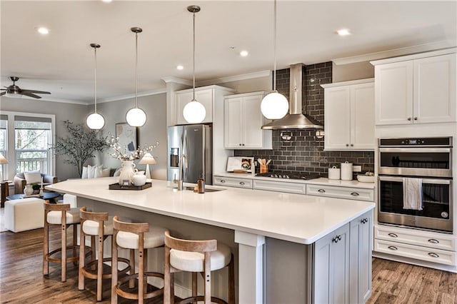 kitchen featuring a large island with sink, decorative backsplash, appliances with stainless steel finishes, wall chimney exhaust hood, and open floor plan