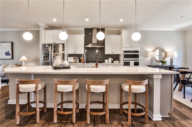 kitchen with a spacious island, backsplash, wall chimney range hood, appliances with stainless steel finishes, and white cabinets