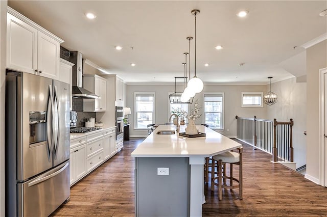 kitchen with a kitchen island with sink, a sink, stainless steel appliances, wall chimney range hood, and dark wood-style flooring