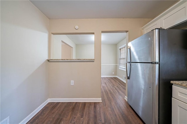 kitchen with light stone countertops, white cabinets, dark hardwood / wood-style floors, and stainless steel refrigerator