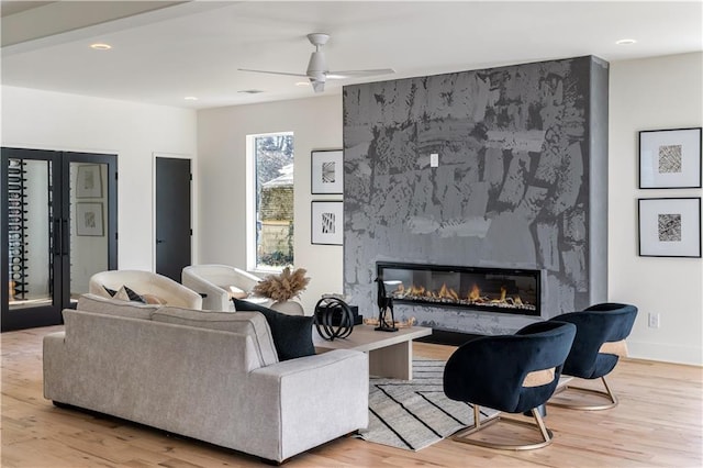 living area with a fireplace, light wood-style flooring, baseboards, and ceiling fan