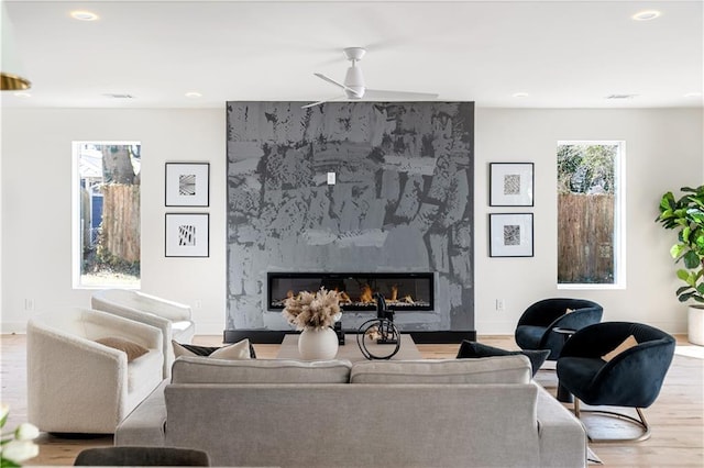 living room featuring ceiling fan, light wood finished floors, a fireplace, and baseboards