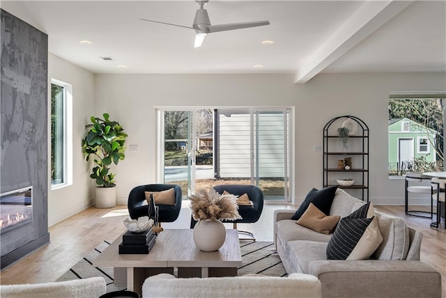 living room featuring light wood finished floors, a large fireplace, baseboards, ceiling fan, and beam ceiling