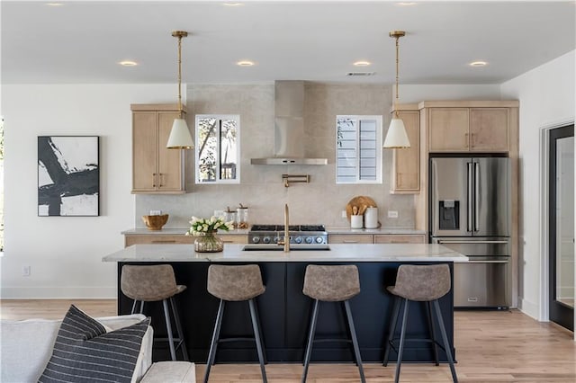 kitchen with wall chimney exhaust hood, light brown cabinets, high end fridge, and decorative light fixtures