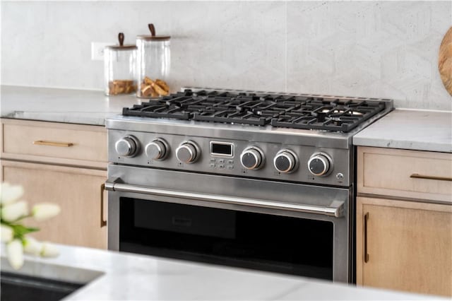 kitchen featuring stainless steel stove, light countertops, backsplash, and light brown cabinets