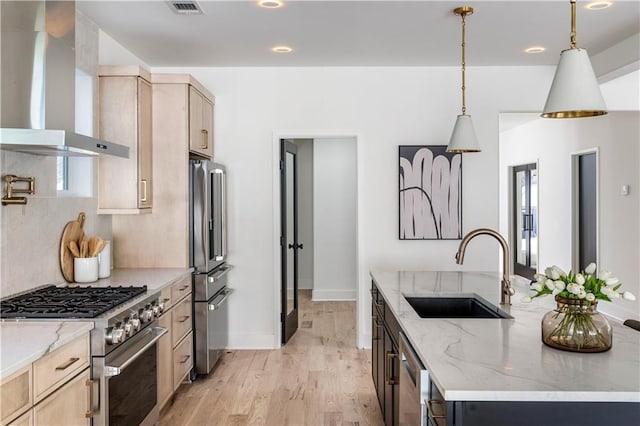 kitchen with premium appliances, light stone counters, light brown cabinets, a sink, and wall chimney exhaust hood