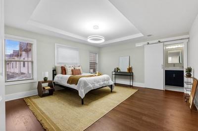 bedroom with a barn door, dark hardwood / wood-style floors, a raised ceiling, and ensuite bathroom