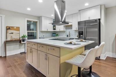 kitchen featuring dark wood-type flooring, wall chimney range hood, a kitchen island, stainless steel fridge, and white cabinets