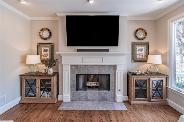 unfurnished living room with a tile fireplace, crown molding, baseboards, and wood finished floors