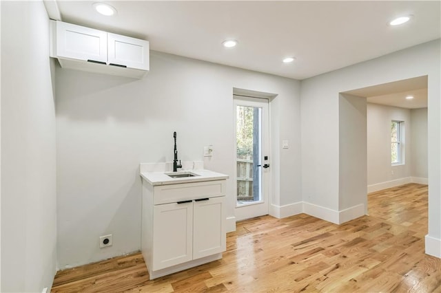 bar with white cabinets, light wood-type flooring, a healthy amount of sunlight, and sink