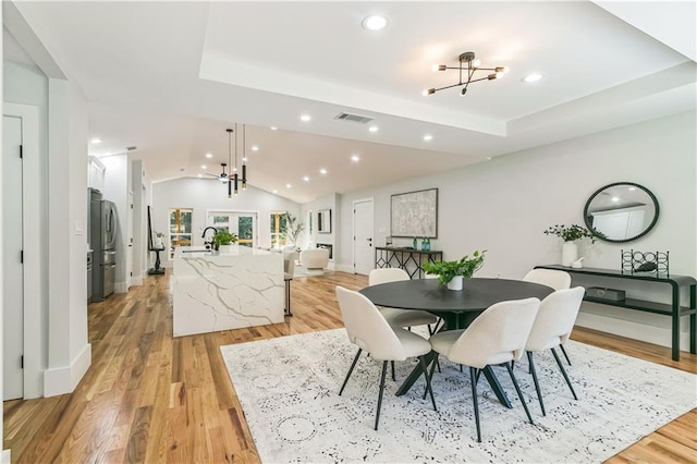 dining room featuring sink, light wood-type flooring, a chandelier, and a tray ceiling