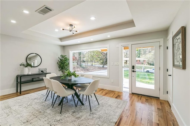 dining room featuring light hardwood / wood-style flooring, an inviting chandelier, and a raised ceiling