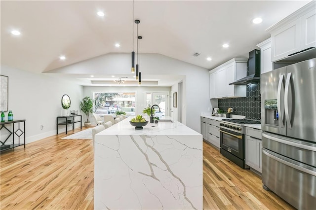 kitchen with wall chimney exhaust hood, stainless steel refrigerator with ice dispenser, a center island with sink, gas range, and pendant lighting