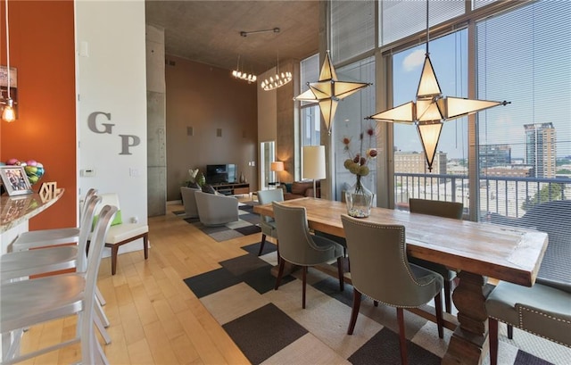 dining area featuring light hardwood / wood-style flooring, a wall of windows, an inviting chandelier, and a high ceiling