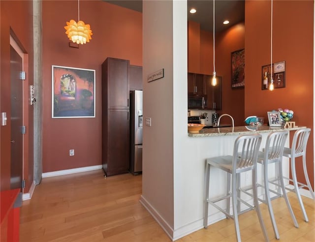 kitchen featuring appliances with stainless steel finishes, light hardwood / wood-style floors, kitchen peninsula, light stone countertops, and a high ceiling