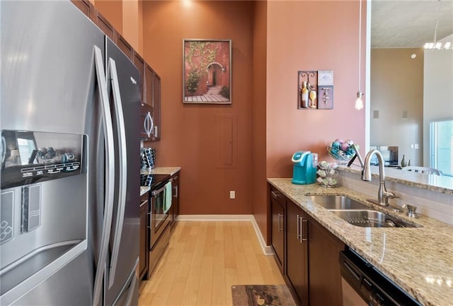 kitchen with stainless steel appliances, a notable chandelier, light hardwood / wood-style flooring, sink, and light stone counters