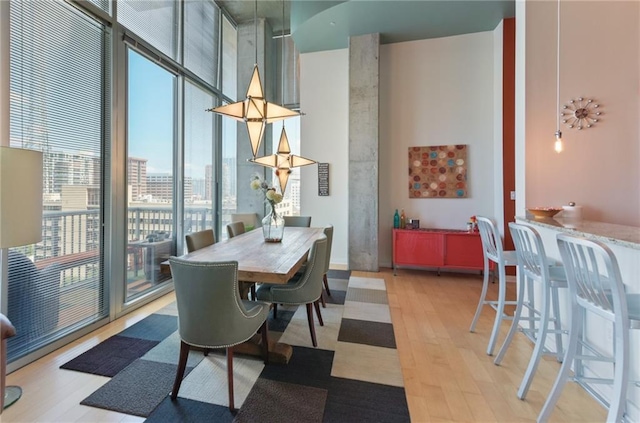 dining room featuring a towering ceiling, a wall of windows, and light wood-type flooring