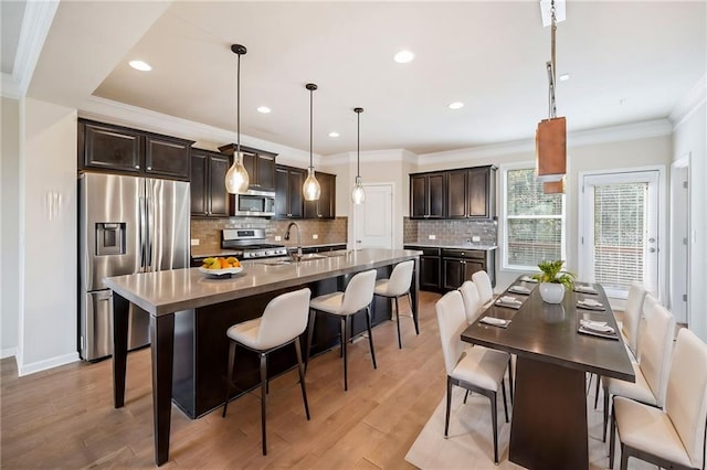 kitchen featuring stainless steel appliances, a kitchen breakfast bar, hanging light fixtures, a kitchen island with sink, and dark brown cabinets