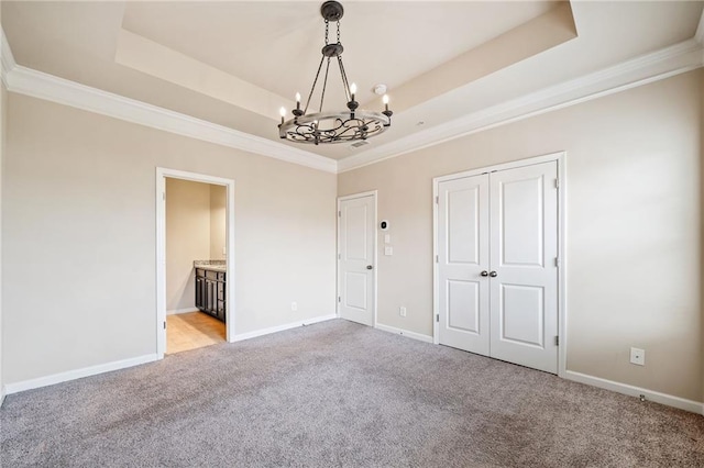 unfurnished bedroom with connected bathroom, an inviting chandelier, ornamental molding, light colored carpet, and a tray ceiling