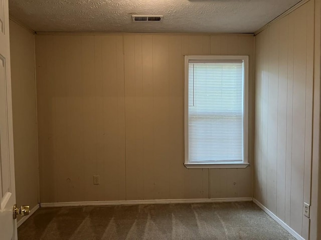 empty room with wood walls, dark colored carpet, and a textured ceiling